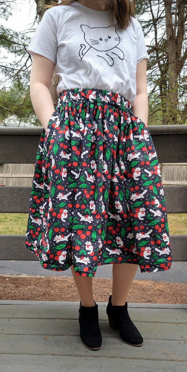 Black skirt with pockets patterned with cats and cherries. Midi skirt below knee length
