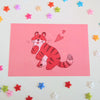 postcard mini print of a red tiger posing cutely and smiling with a pink background
