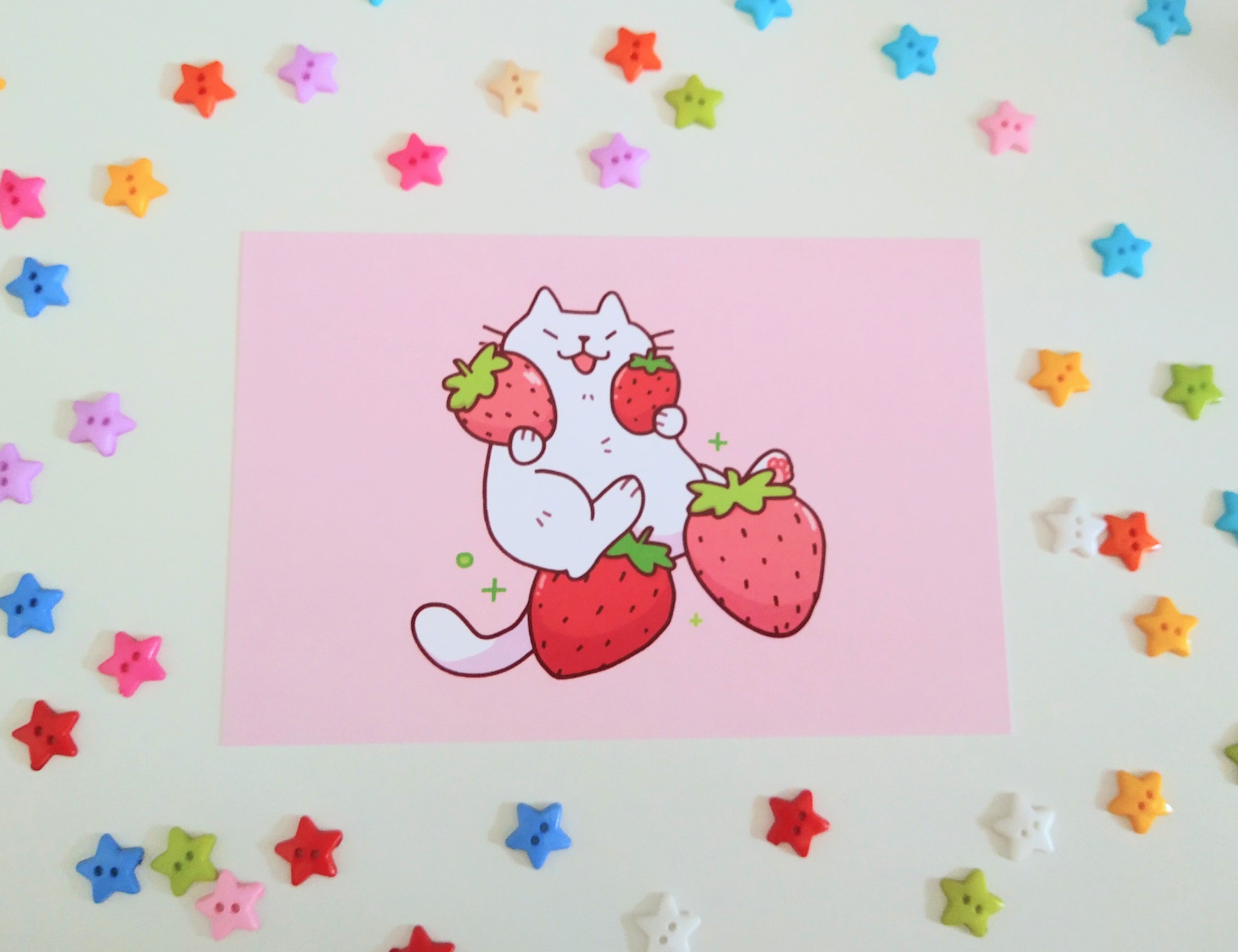 postcard mini print of a white cat holding strawberries with a pink background, drawn in a cute style