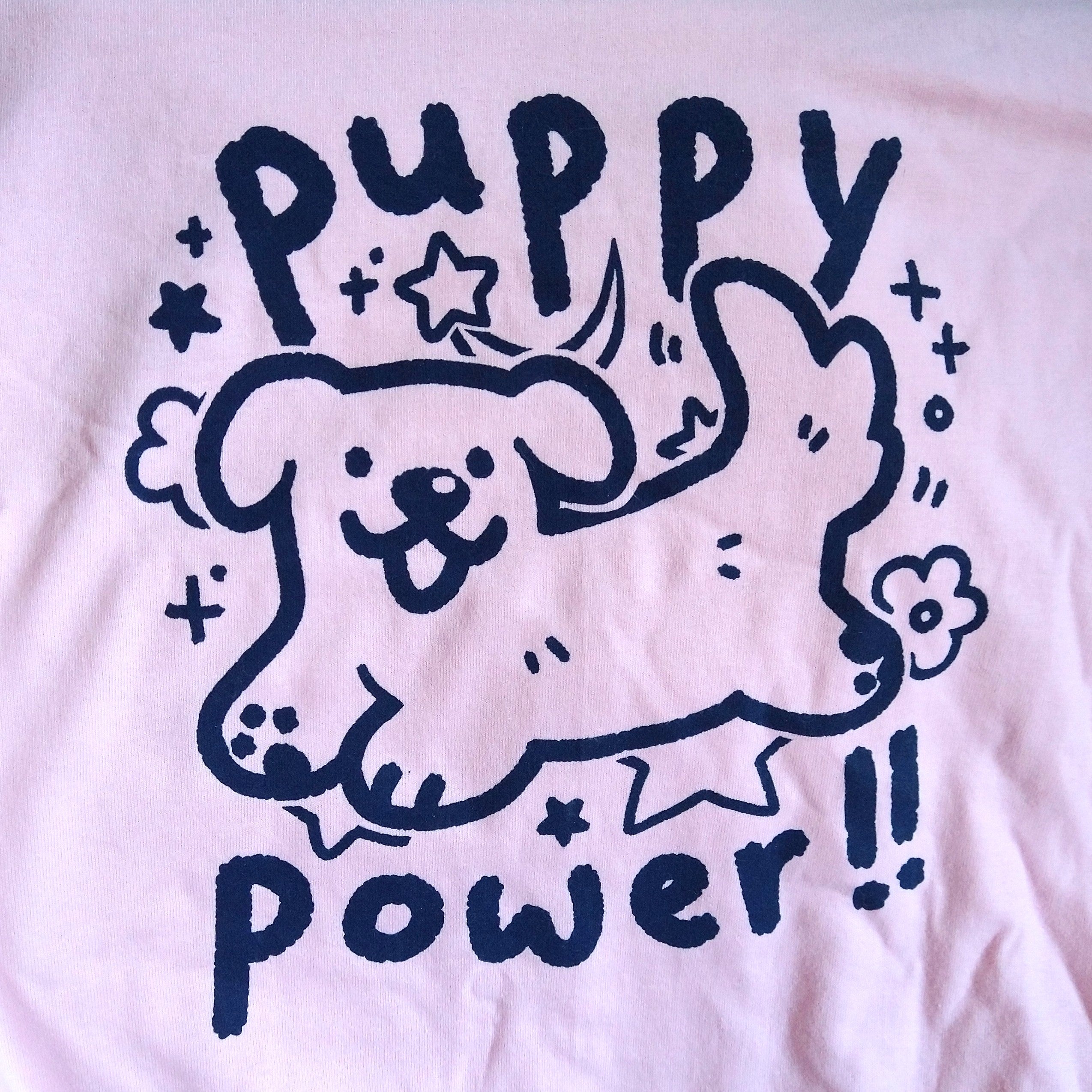 pink graphic tee printed with cute drawing of a dog with a shiny nose surrounded by flowers and stars. text reads "puppy power!!"