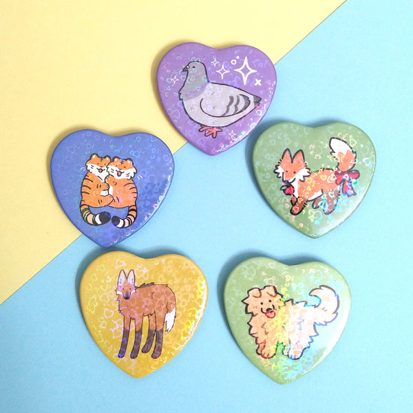 5 heart-shaped pinback buttons featuring pigeon, red fox, dog, maned wolf, and tigers, all holographic