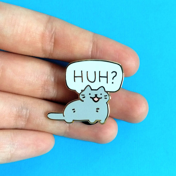 Gold plated hard enamel pin of gray cat with speech bubble "HUH?"