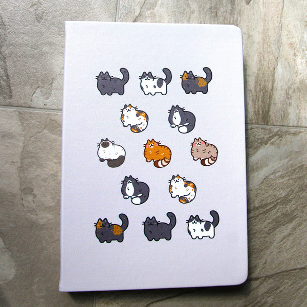 Gray notebook cover featuring many cute cats of various coat colors including black, cow/spotted, tortoiseshell, calico, tuxedo, seal point Siamese, orange tabby, and brown tabby.