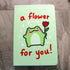 Light green notebook cover featuring a kawaii frog with rosy cheeks holding up a red tulip. Text reads "a flower for you!" in red handwritten lettering