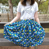 Blue skirt patterned with white cats and lemons. The skirt is midi length and ends below knee.