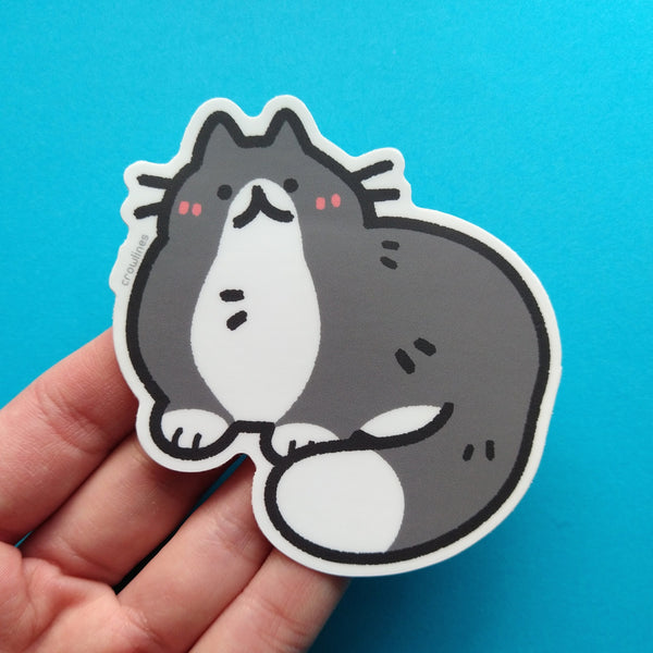 Sticker of a black and white cat, a tuxedo cat. The cat is drawn in a cute style and is very round.