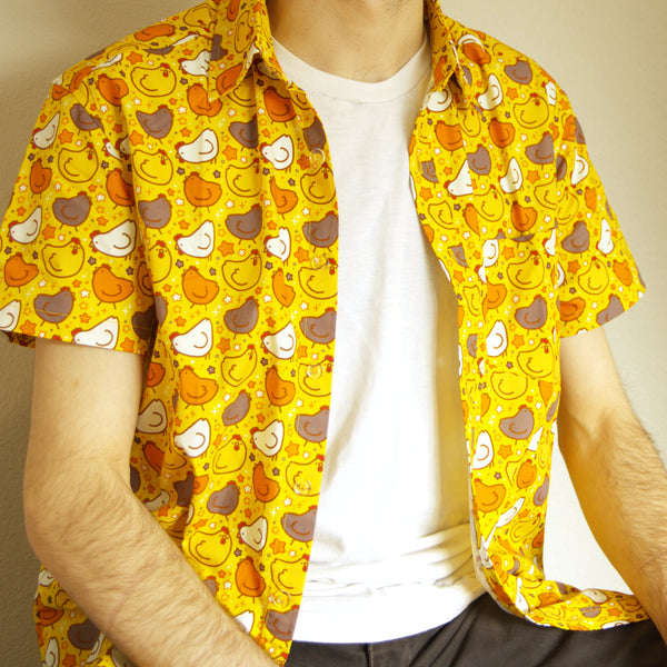 yellow button up shirt patterned with chickens and stars, worn unbuttoned over a plain white tee