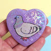 purple heart-shaped pinback button with drawing of a pigeon, layered with a holographic heart film