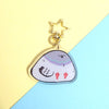 clear acrylic keychain of a comically round and wide pigeon sitting on its butt, with a gold star-shaped clasp