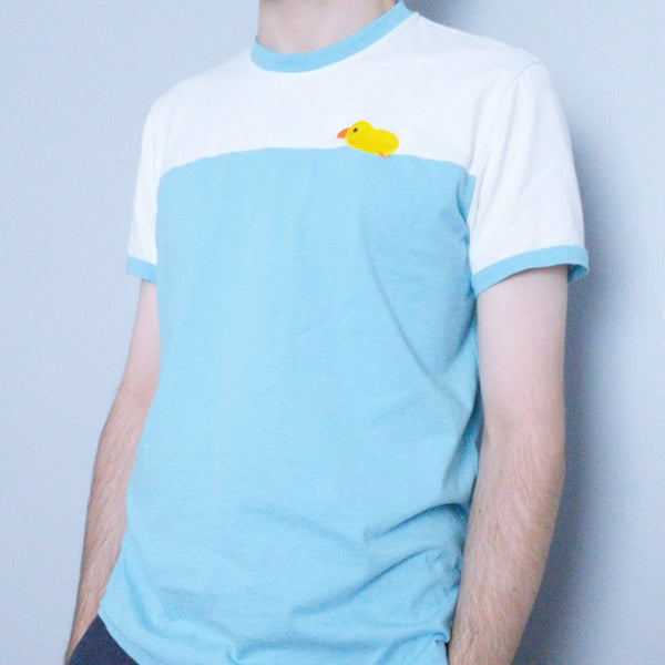 Modeled photo of ringer tee with light blue trim on collar and sleeves. Chest has embroidery of a cute duck