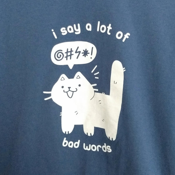 Blue shirt with screen printed graphic of a white cat drawn in a cute style. The cat has a censored speech bubble. Text reads "I say a lot of bad words"