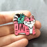 Gold plated hard enamel pin of a pink tiger with plants behind it