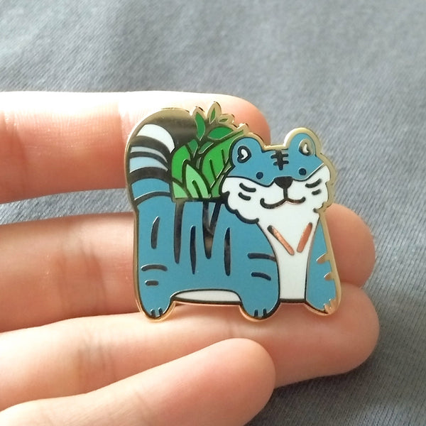 Gold plated hard enamel pin of a blue tiger with plants behind it