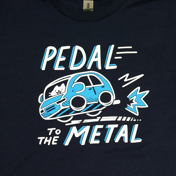 Navy blue t shirt printed with graphic of a cat driving a cartoonish blue car, with tire skid marks. Text reads "PEDAL TO THE METAL"