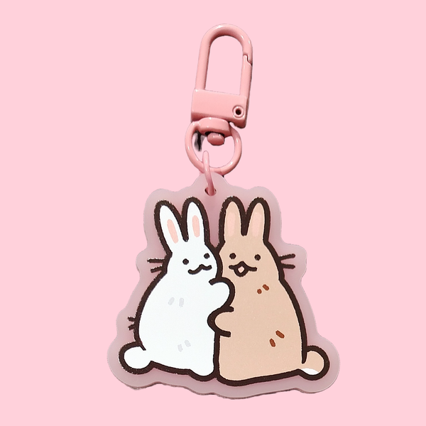 Keychain of a pair of bunnies hugging. There is a white bunny and a brown bunny. The keychain has a pink clasp.