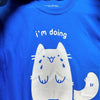 Bright blue tee screen printed with graphic of a crying white cat. Text reads "I'm doing my best"